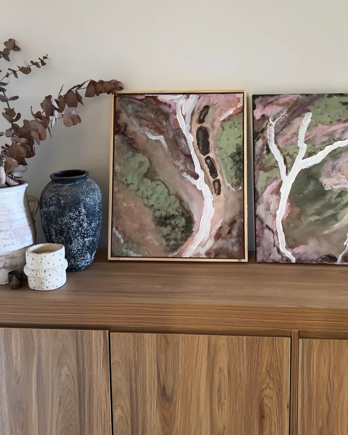 Shop all art. Two framed original landscape paintings by Ally McCann displayed on a wooden sideboard.